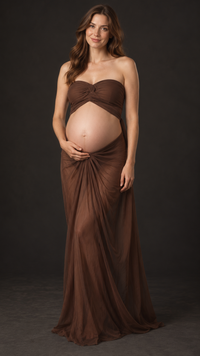 Pregnant woman in a chocolate brown strapless ruched top and long sheer draped skirt against a dark studio backdrop