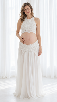 Pregnant woman in a white lace halter crop top and long flowing skirt in a bright white studio