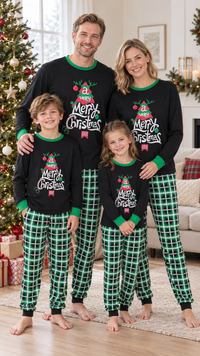 Family in matching black Christmas pajama tops with a decorated tree and white Merry Christmas script, worn with green plaid pants.