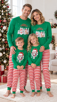 Family in matching green Christmas pajama tops with a snowy village graphic, worn with red and white striped pants.