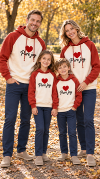 Family of four in matching cream hoodies with brick-red raglan sleeves and hoods, printed with a red heart and the words Pure joy.