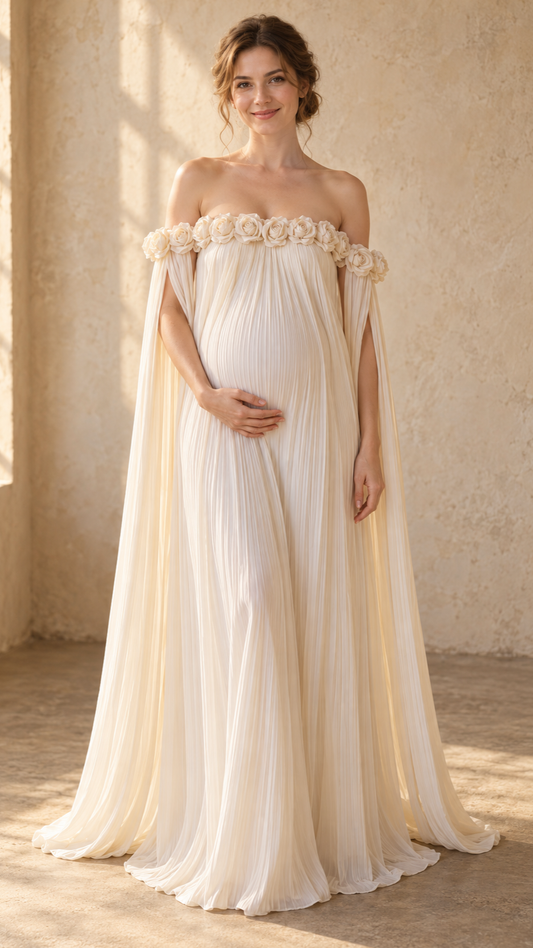 Pregnant woman in an ivory pleated off-shoulder maternity dress with rosette trim in a candlelit room