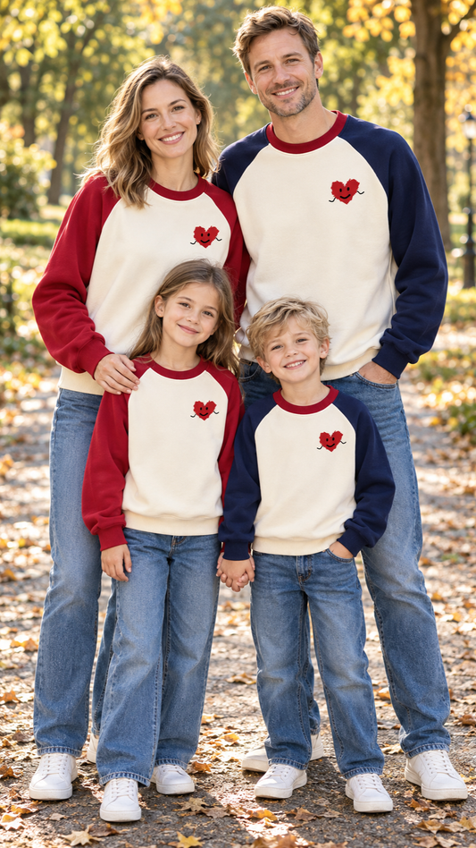 Family in matching cream sweatshirts with navy or red raglan sleeves and a small smiling red heart on the chest.
