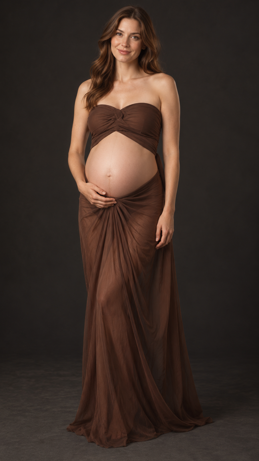 Pregnant woman in a chocolate brown strapless ruched top and long sheer draped skirt against a dark studio backdrop