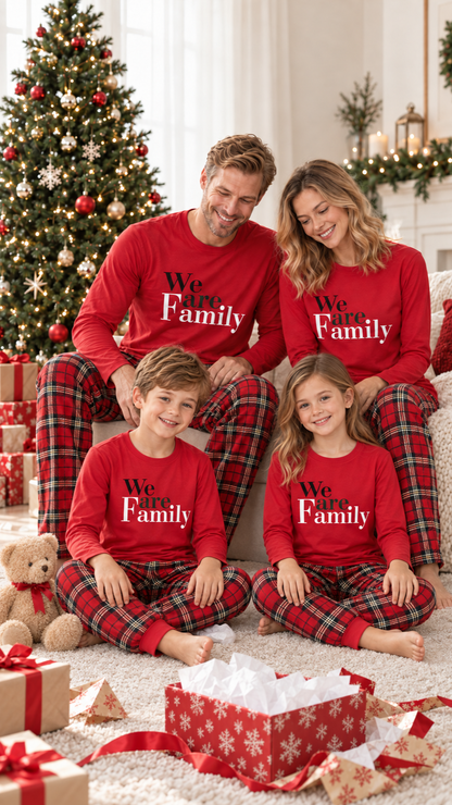 Family in matching We Are Family Red Christmas pajamas on Christmas morning by the tree.