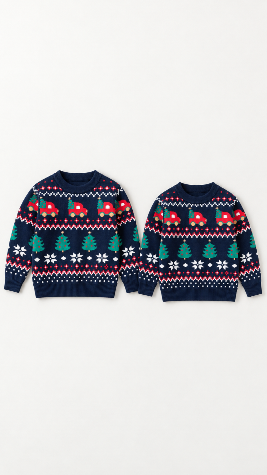 Two dark blue Fair Isle kids' Christmas sweaters with red trucks, Christmas trees and snowflakes, laid flat.