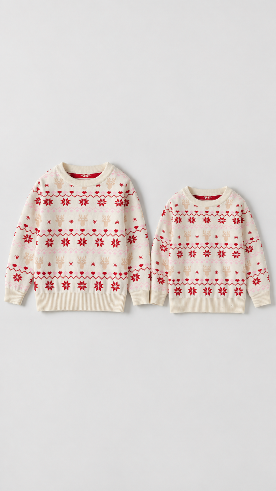 Two cream Fair Isle kids' Christmas sweaters with reindeer, red snowflakes and pink hearts, laid flat.