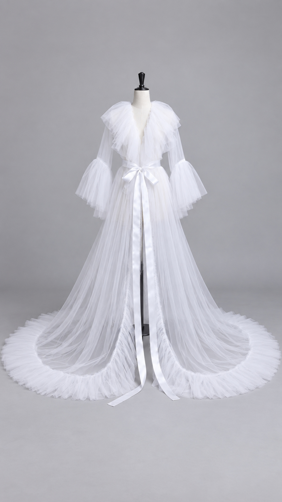 White sheer tulle maternity gown with a ruffled V collar and satin sash on a dress form