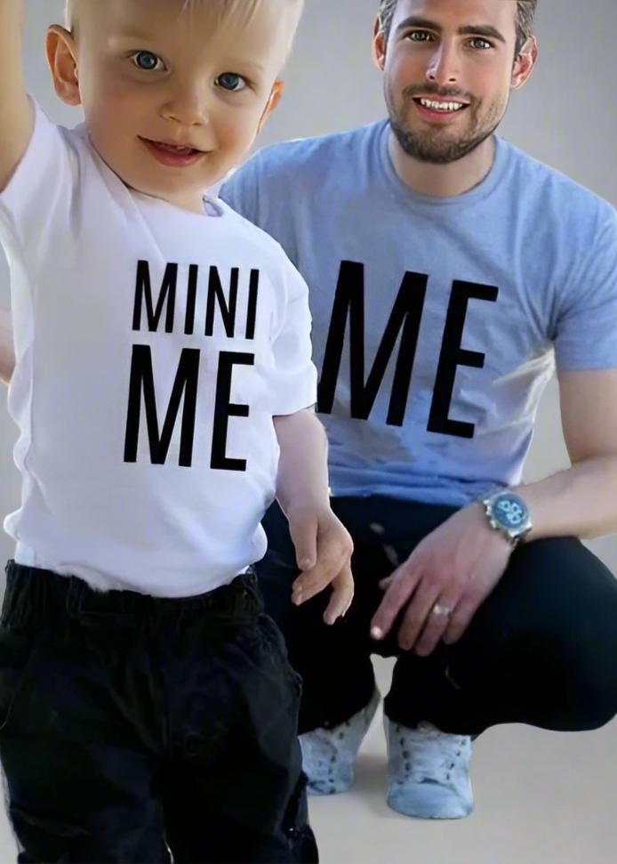 Father and son wearing matching 'Me' and 'Mini Me' shirts, dad in gray and child in white