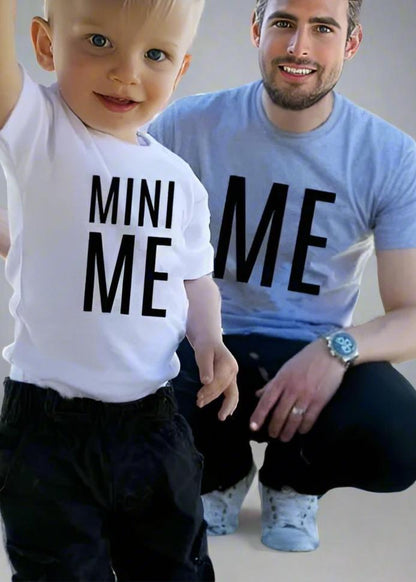 Father and son wearing matching 'Me' and 'Mini Me' shirts, dad in gray and child in white